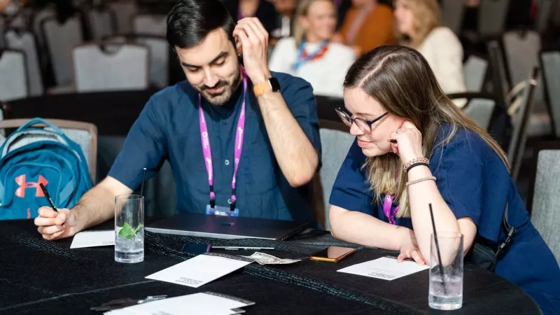 A man and woman are sitting at a table, working on their laptops at Cvent CONNECT 2023.