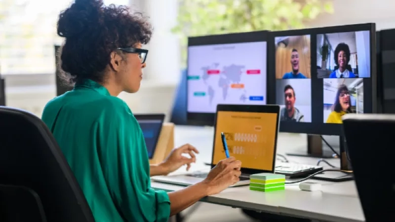 A woman sitting at her desk with a laptop and monitor in front of her in an office.