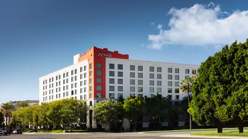 Exterior view of Zessa hotel with its distinctive red and white facade, surrounded by trees.