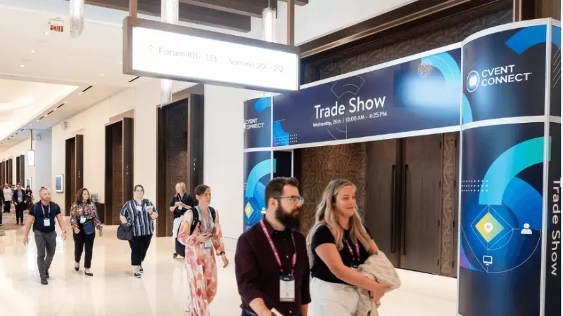 People walk through a corridor with an informational sign for a trade show.