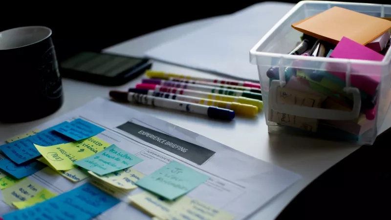 Post-it notes, pens, and a smartphone on a desk for an experience briefing.