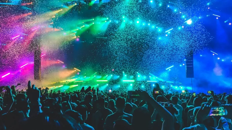 A crowd of people at a concert with colorful lights and confetti in the air.