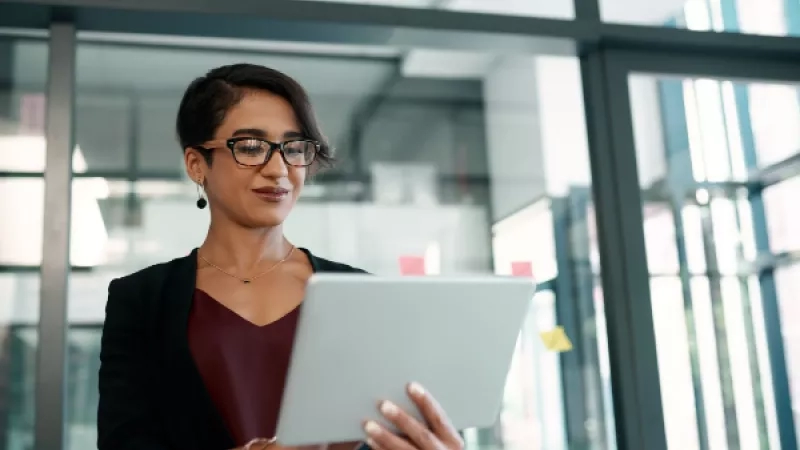 Female standing in an office holding a tablet and looking at the camera with a smile.