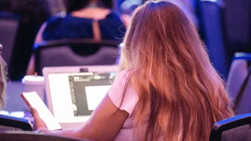A woman using her phone next to her laptop during an event at a conference center.