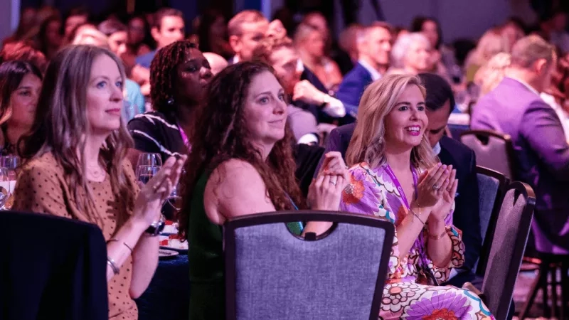 Audience members at an event with one woman clapping her hands and smiling for the camera.