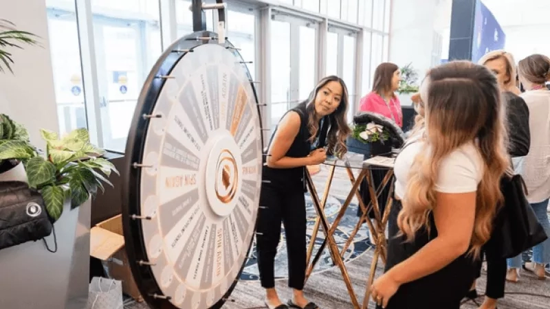 A woman spins a wheel at a pop-up event with a backdrop of glass and greenery.