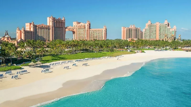 Atlantis Bahamas with beach and ocean view with rows of chairs on the beach and trees and buildings.