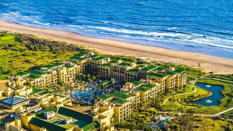 Aerial view of Quinta da Marinha Resort, featuring yellow architecture, green roofs, and lush landscaping by the ocean.