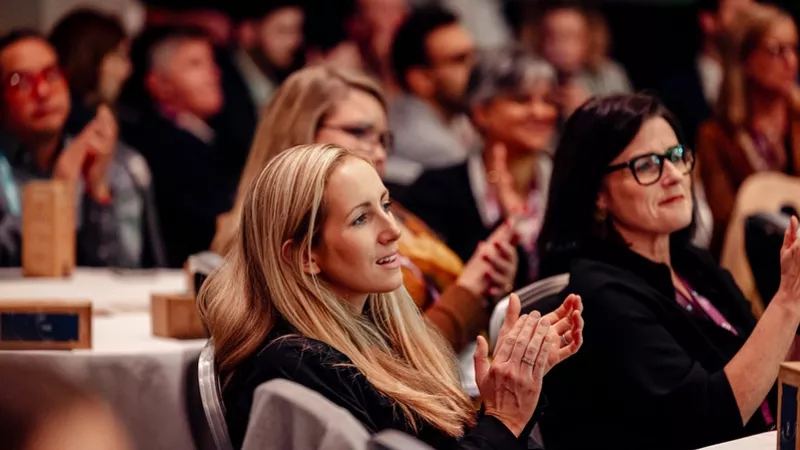 Group of people attending a B2B event, with two women in the foreground clapping their hands.