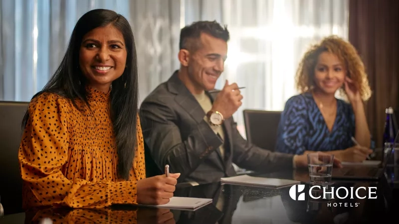 Three people in a conference room at Choice Hotels, with a logo in the bottom right corner.