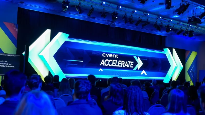 A crowd gathered in a conference hall with a blue-lit stage displaying the words "Cvent Accelerate".