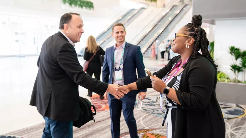 Two people shake hands in a large lobby with a third person standing nearby at HIMSS23 in Chicago.