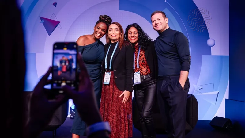 Three women and a man are smiling while a person is taking a photo of them.