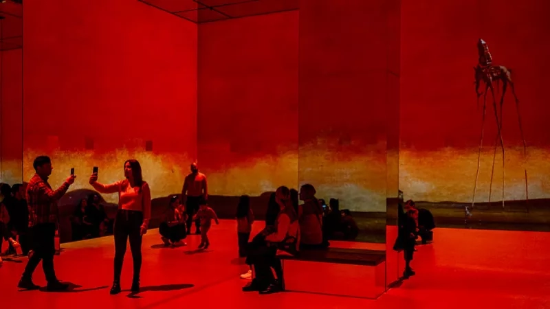 People inside the Dali museum, standing and taking pictures in front of the large red Dali mural.