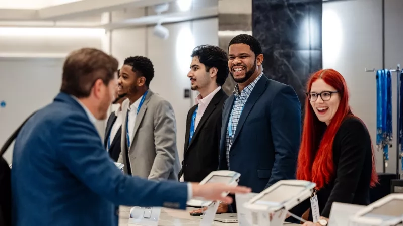 A group of attendees smiling and checking in at a conference registration desk with digital kiosks.