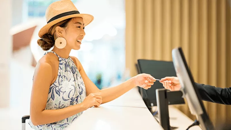 A woman receives a room key from a hotel staff member at the front desk.