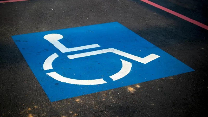 Wheelchair parking sign on a blue square on a parking lot floor.