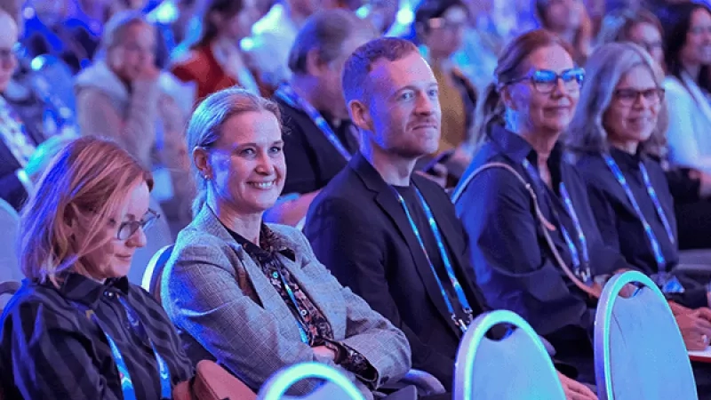 Group of attendees sit in chairs at a meeting with blue light.