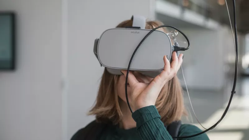 A woman wearing an Oculus VR headset in an office, with cables attached to the headset.