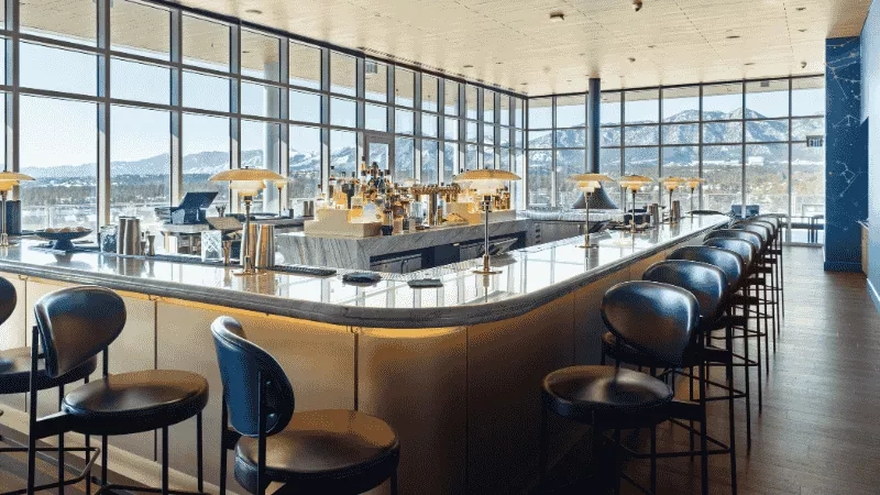 Interior of a bar with wooden floors, glass windows, and mountains in the background.
