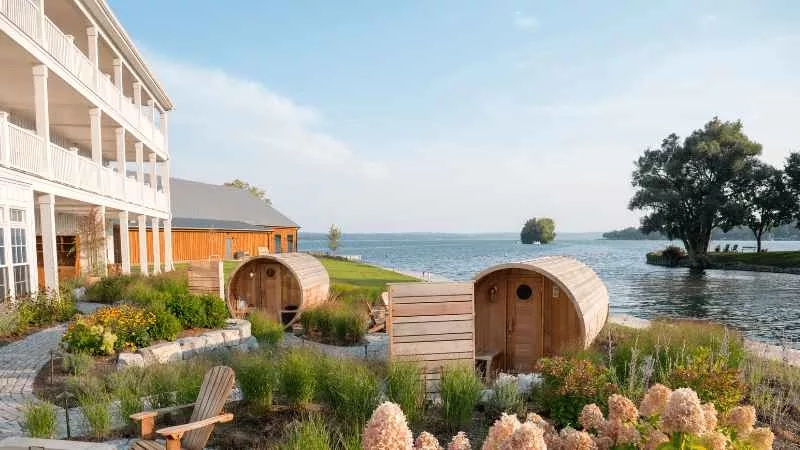 Wooden cabins near a building with a balcony and lake view in the background.