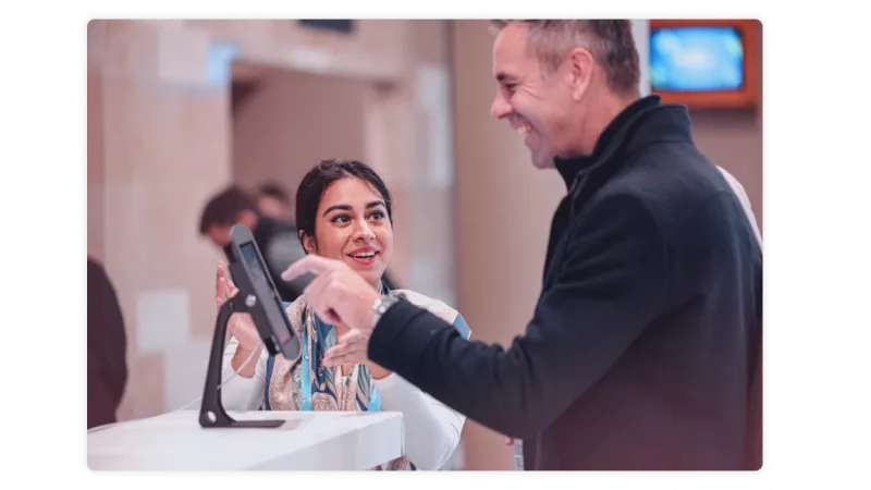 A woman is standing at a counter while a man in a black jacket speaks with her.