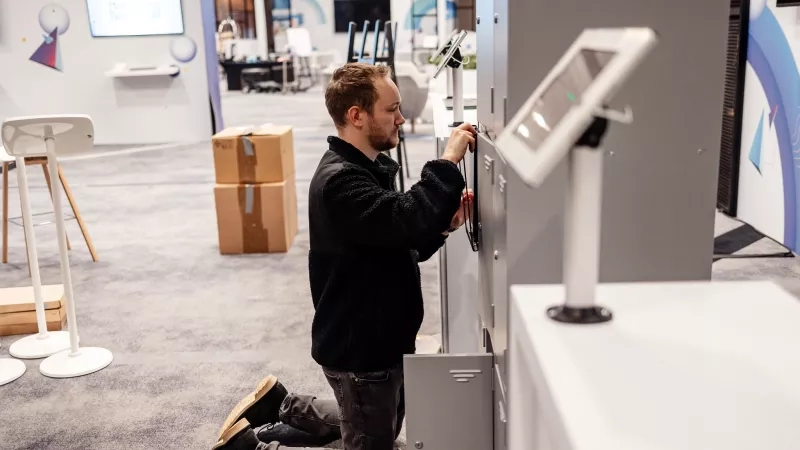 Man setting up Cvent CONNECT Europe 2024 event in a room with chairs, monitors, and boxes.