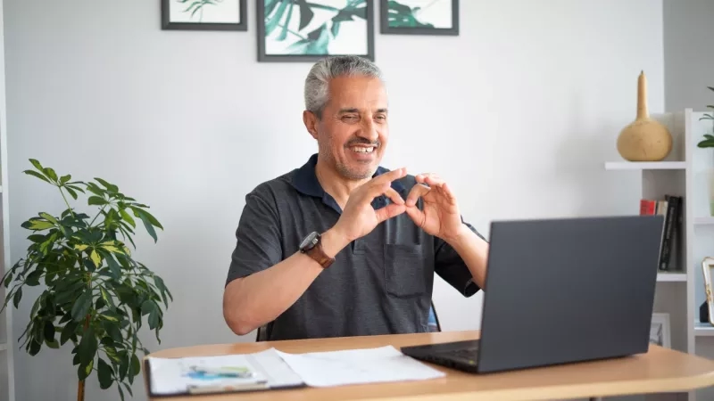 A man is sitting at a desk with a laptop and smiling.
