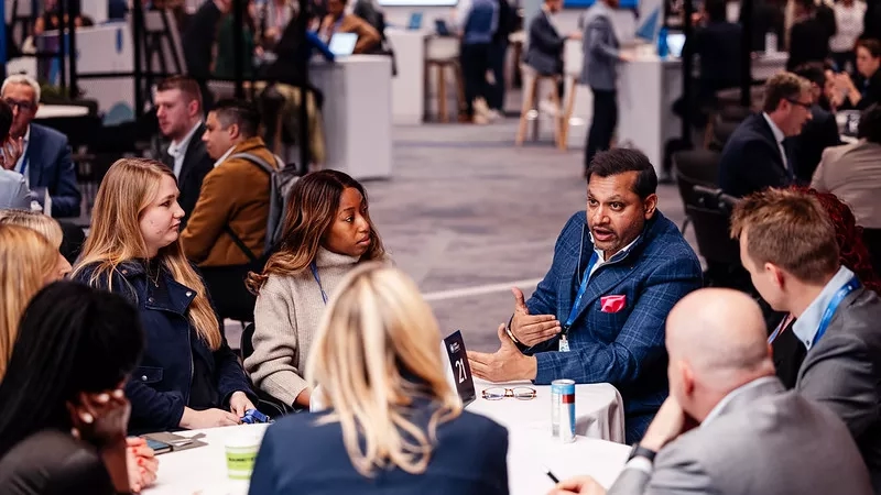 A man is speaking to a group of people sitting around a table in an office.