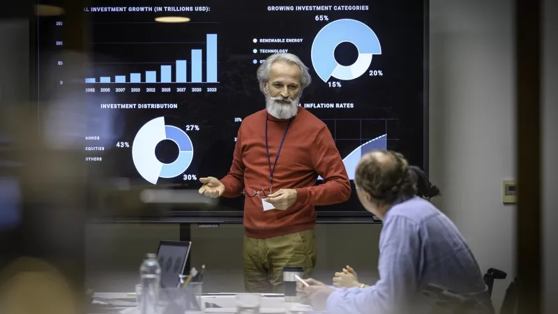 Businessman doing presentation in front of colleagues at conference room with graphs on the screen.