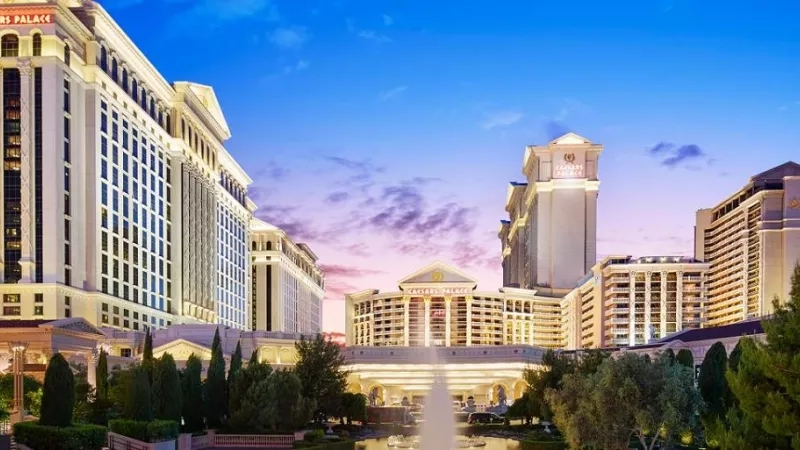 Dusk view of Caesars Palace, Las Vegas, with buildings, trees, and a fountain in the foreground.