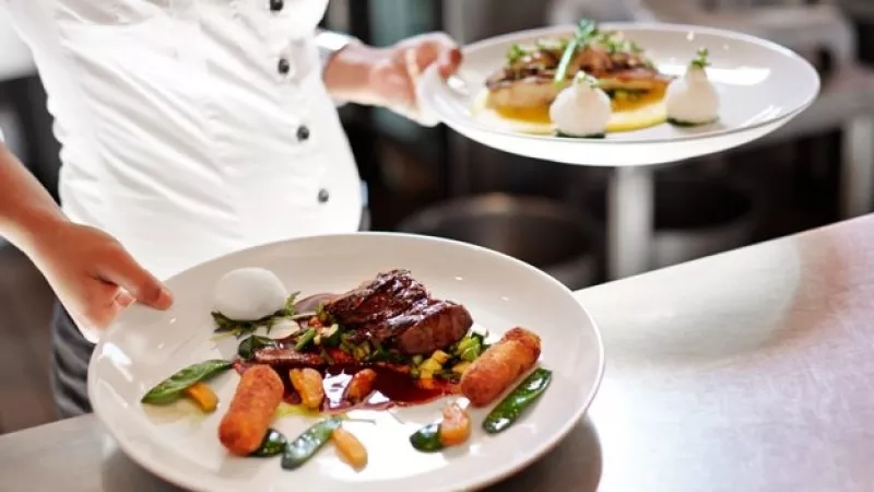 A chef holding a plate of food and another plate of food sitting on a table.