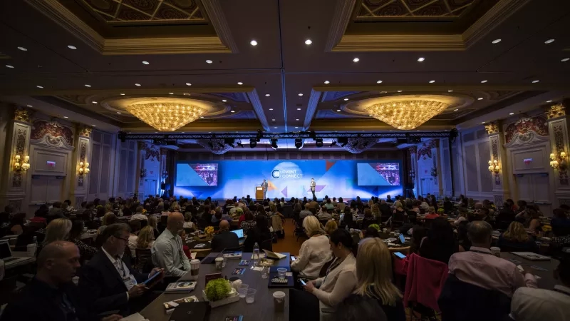 A large room with people sitting in chairs and a screen displaying "Cvent Connect" on it.