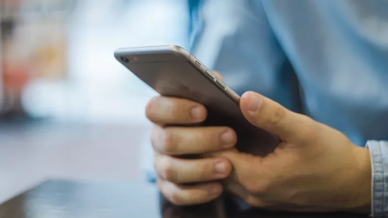 Person's hands holding a smartphone and blurred background of a table and restaurant setting.