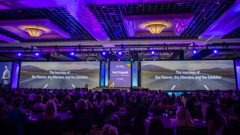 Cvent Connect attendees in an auditorium with three large screens displaying "The Journeys of" in purple and orange.