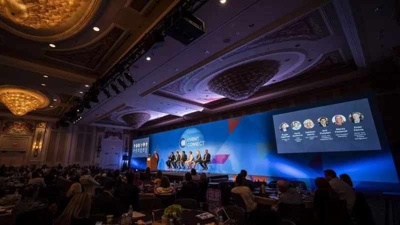 Group of people in an auditorium listening to a speaker in a presentation with a large screen behind.
