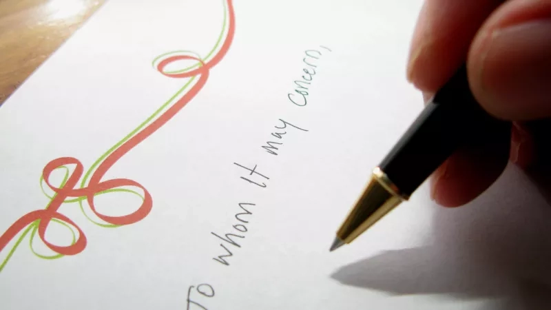 A hand holding a pen is writing on a piece of paper that reads "To whom it may concern."