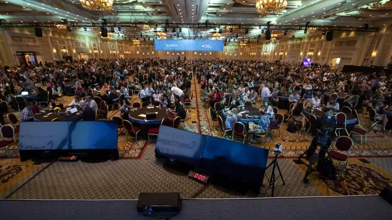 Large crowd at a conference in a large room with monitors and cameras on the floor.