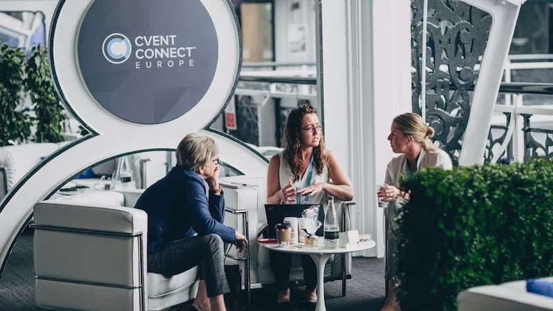 Three people sit on white chairs with the Event Connect Europe logo in the background.