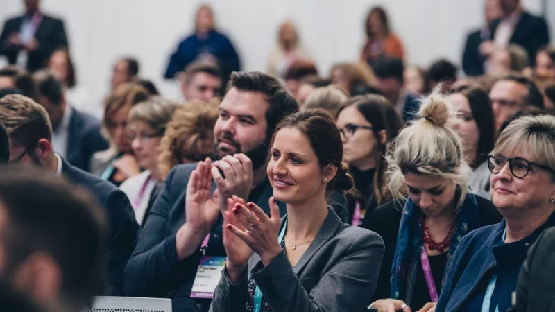 Woman in a suit clapping hands in a crowd of people in a conference room.