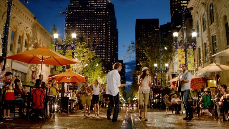 People standing and sitting around tables and umbrellas at night on a city street in Calgary, Alberta.