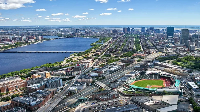 An aerial view of Fenway Park in Boston, surrounded by urban architecture and a river.