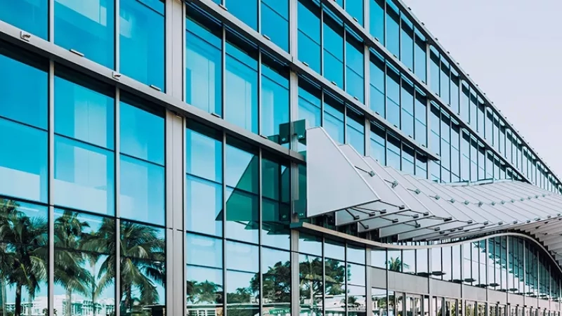 Exterior of a building with a glass wall, a white canopy, and a clear sky above.