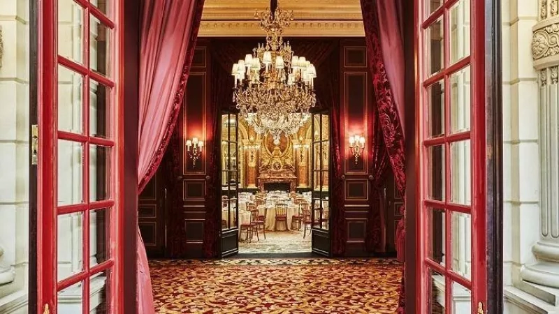 The interior of the Ritz Paris hotel, showcasing an elegant dining area with chandeliers and red curtains.
