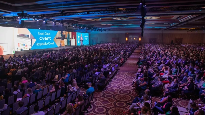 A large conference hall with a stage and a large audience watching the presentation at Event Cloud Cvent.