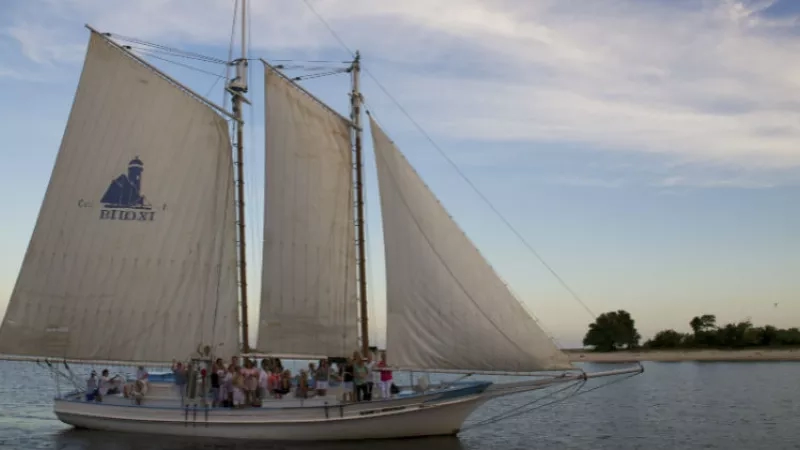 Biloxi Schooner sailing on Mississippi Gulf with a group of people and blue sky in the background.