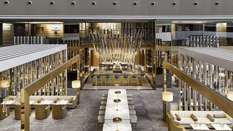 A luxurious restaurant with a high ceiling, a bar, and a large chandelier in the middle.