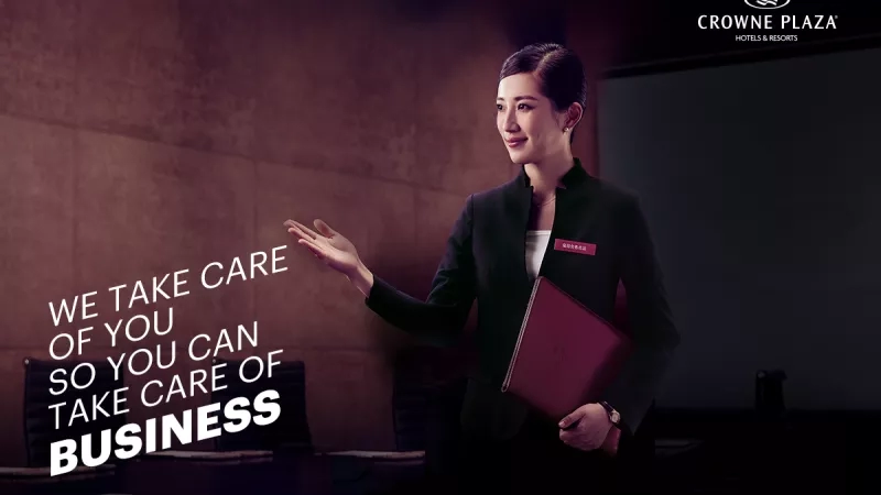 Business meeting room at Crowne Plaza with a woman and text reading "We take care of you".