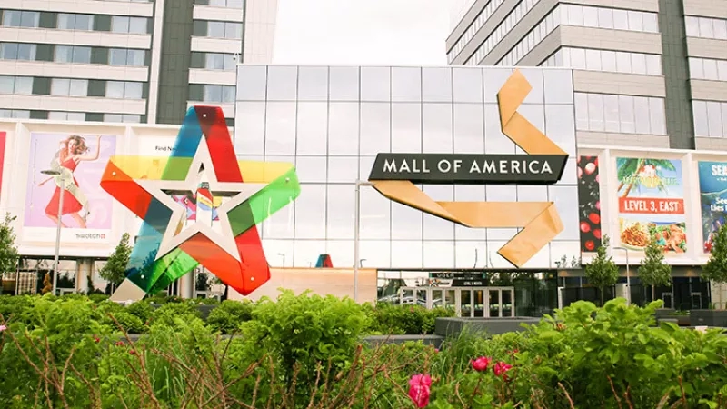 Exterior of Mall of America with a star sculpture and colorful posters, showcasing modern architecture and vibrant landscaping.
