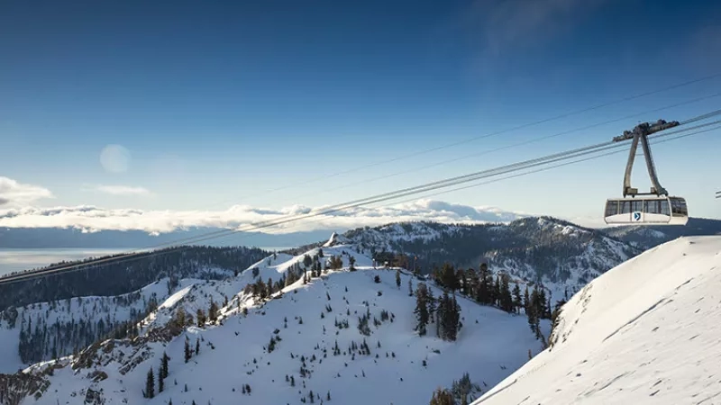 A white cable car with a blue logo descends down the snowy mountain at Squaw Valley.